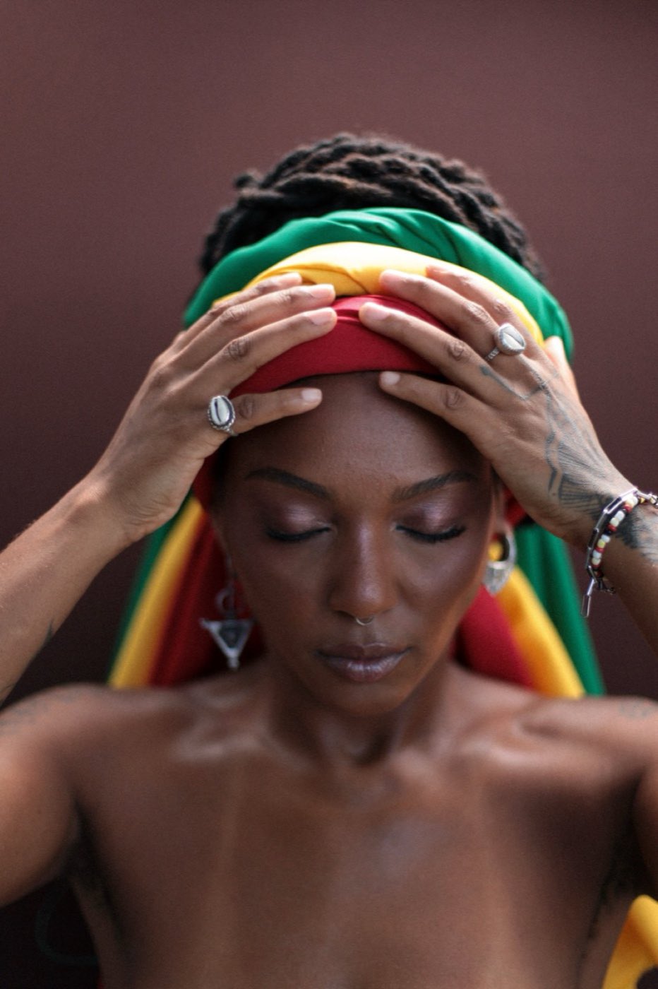Bia Ferreira, eyes closed, hands on a green, yellow and red head wrap