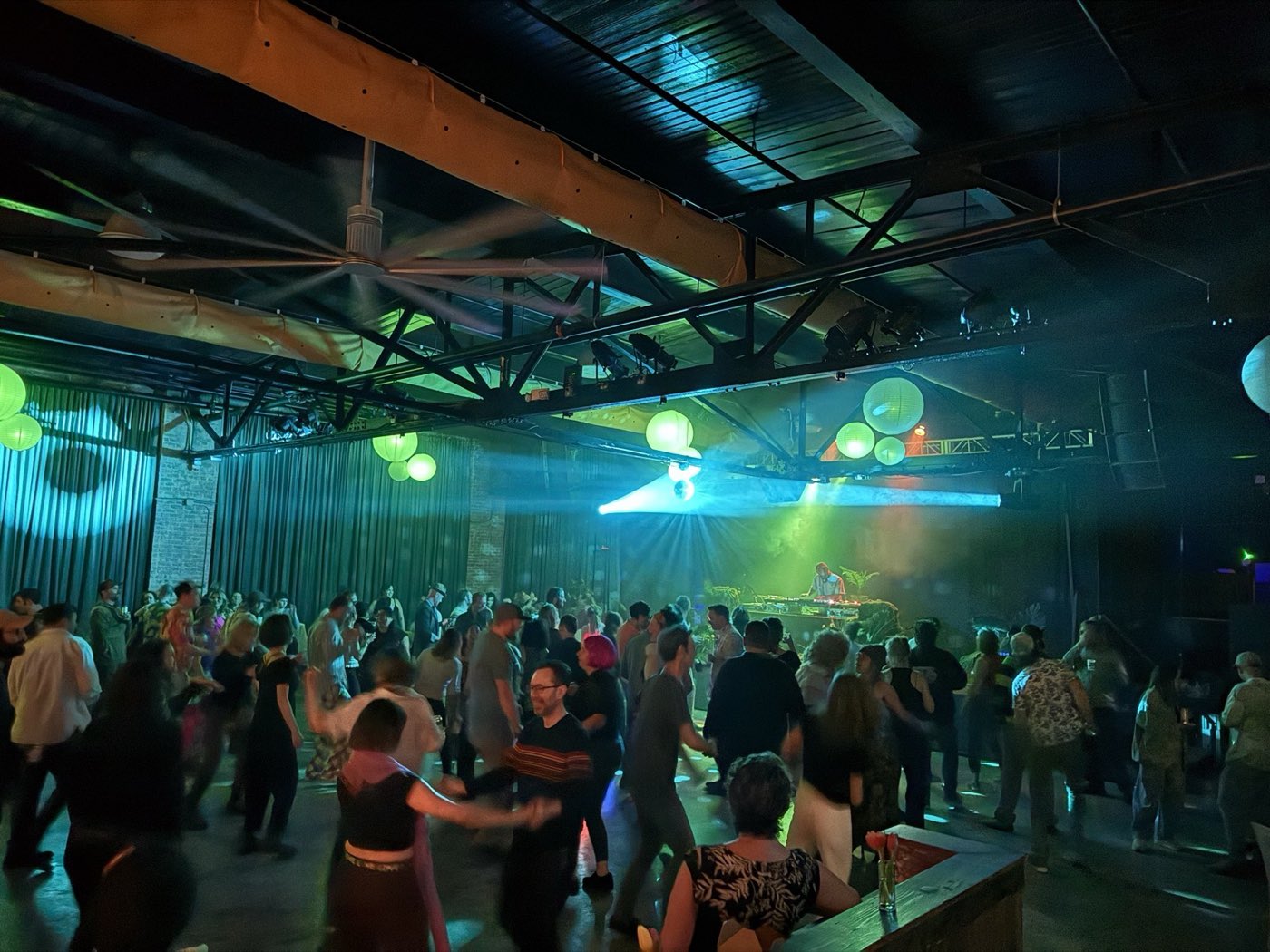 A crowded dance floor under green paper lanterns and teal curtains